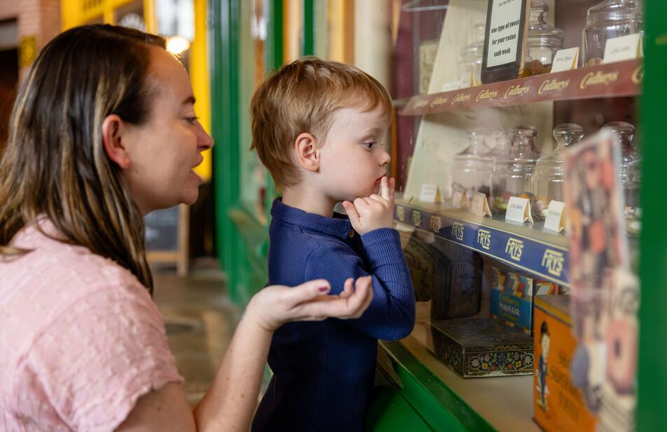 A child looking at sweets in the sweet shop with their mother behind them