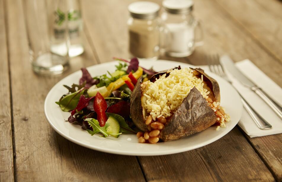 Baked Potato with cheese and beans, and a side salad, served on a table