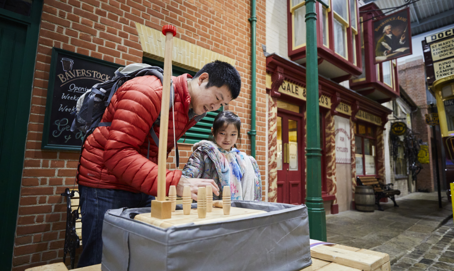 A father accompanies his daughter playing a game on the streets of Milestones