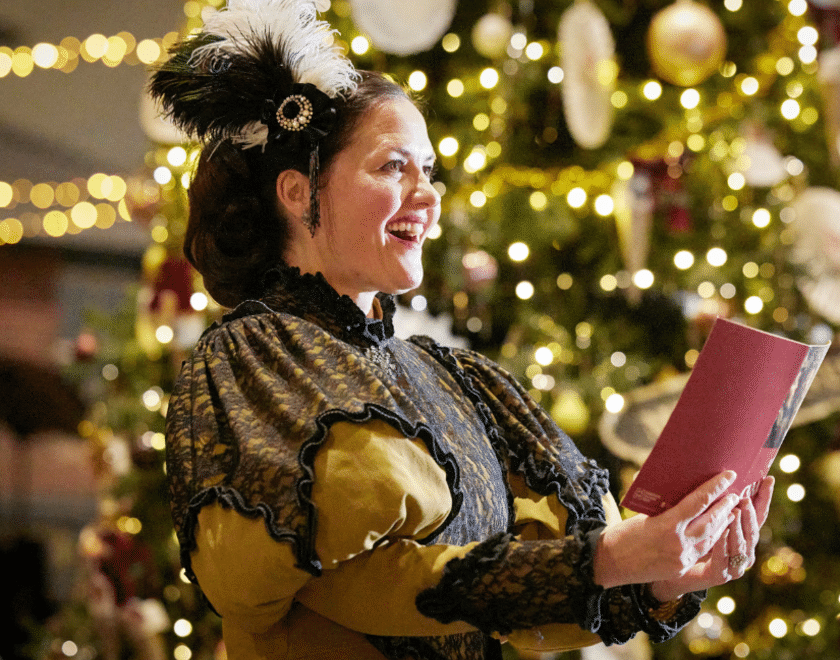 singer in victorian dress in front of Christmas tree
